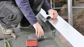 Ein Klempner der auf einem Flachdach arbeitet mit einem Akkubohrer