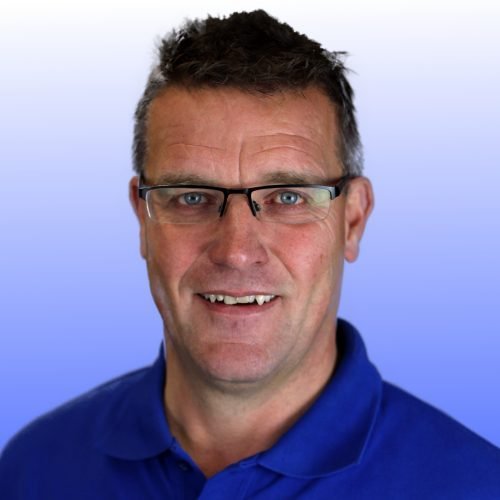 Ein lächelnder Mann mit Brille trägt ein blaues Hemd und hat einen freundlichen Ausdruck auf seinem Gesicht.