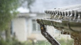 Wassertropfen fließen lebhaft von einem Dachrinnensystem, während ein starker Regen die Umgebung durchnässt.