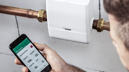 Eine Wassersteuerung und ein Mann der eine App auf dem Smartphone bedient