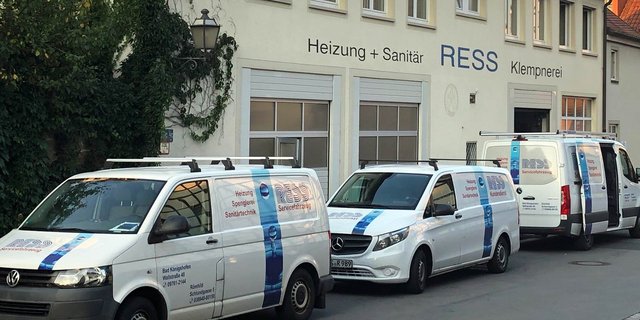 Drei Fahrzeuge mit dem Logo der Firma RESS stehen vor einem Gebäude, das Dienstleistungen in Heizung und Sanitär anbietet.